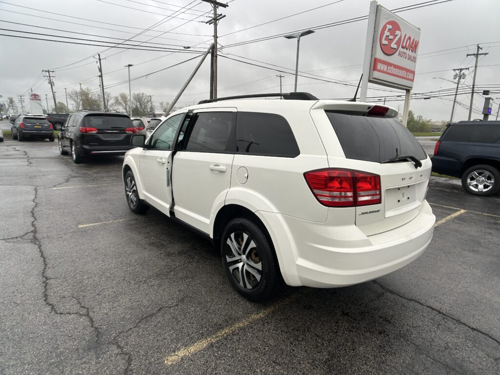 White SUV parked at a car dealership lot with other vehicles and an EZ LOAN sign in the background.