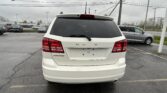 Rear view of a white Dodge Journey in a parking lot, with other cars and power lines visible in the cloudy background.