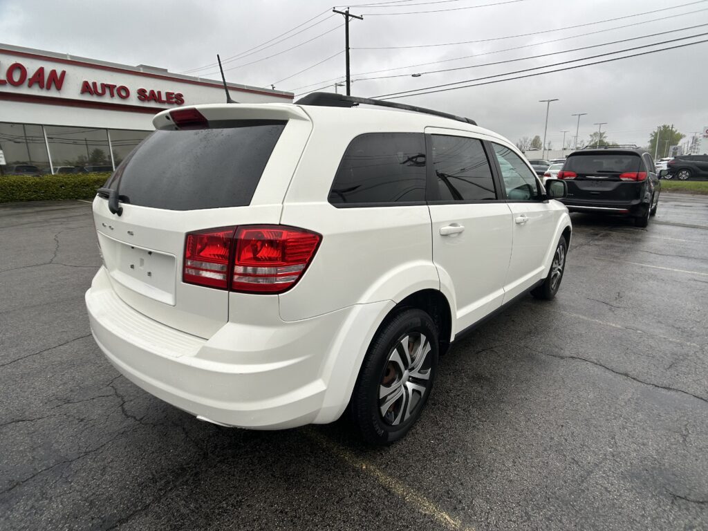 White SUV with roof rails parked in a car lot next to a dealership building with red 'AUTO SALES' signage in the background.