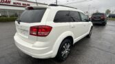 White SUV with roof rails parked in a car lot next to a dealership building with red 'AUTO SALES' signage in the background.
