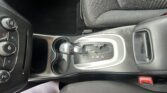 Center console of a car showing an automatic gear shift (P-R-N-D), cup holder, and nearby controls beside a fabric seat.