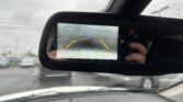 Rearview mirror display showing parking guidance lines (green/yellow/red) as raining scene passes by outside the car window.