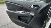 Car door interior panel with chrome handle, window controls, and speaker grille; parking lot outside visible through window.