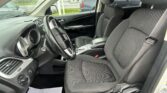 Interior view of a car's front seats, steering wheel, dashboard, and center console from the passenger side door with exterior cars visible outside the windows.