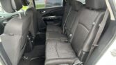 Rear row of black cloth seats in an SUV, with three headrests, seat belts, and door panel visible from the open rear door.