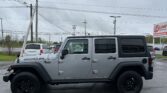 Silver Jeep Wrangler SUV parked in a lot with utility poles and overhead power lines, and an EZ LOAN Auto Sales sign in the background.