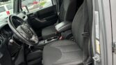 Open car door view of a black interior: front seats, steering wheel, center console, and dashboard in a parking lot outside.