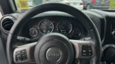 Steering wheel with Jeep logo and dashboard gauges, view of a crowded parking lot through the windshield.