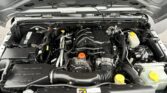 Under-hood view of a Jeep engine bay with various hoses, wires, and the battery visible on the left; Jeep grille at the bottom edge.