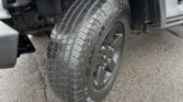 Close-up of a pickup truck's front left wheel, showing the treaded tire and black fender with an orange side marker light.