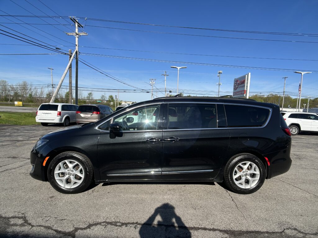 Black SUV in the foreground at a car dealership lot, with other vehicles and power lines overhead against a clear blue sky.