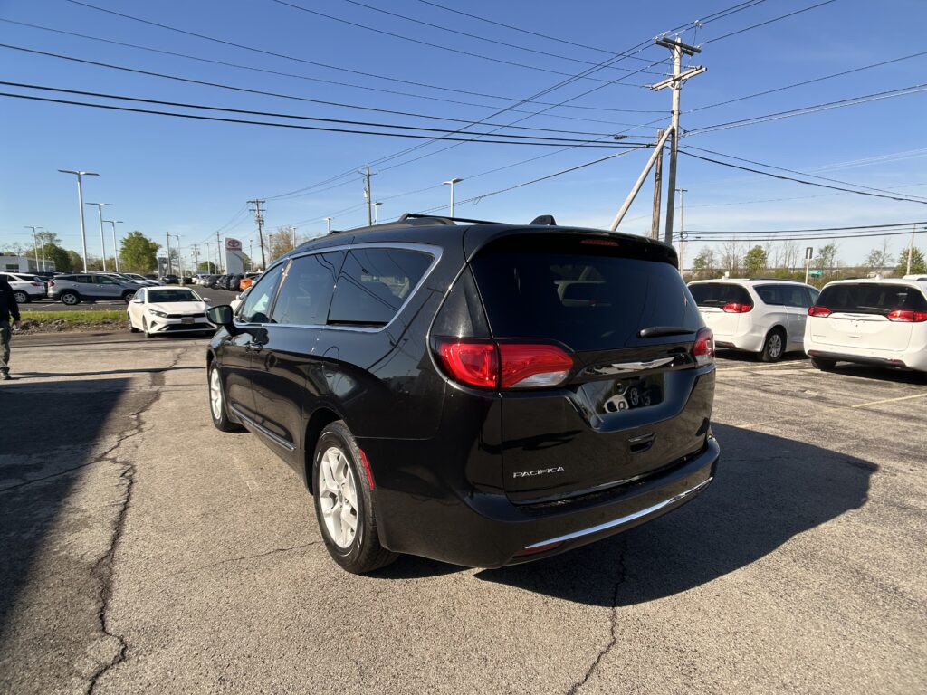 Rear view of a black Chrysler Pacifica minivan in a car dealership lot, with white cars and power lines overhead.