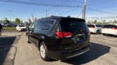 Rear view of a black Chrysler Pacifica minivan in a car dealership lot, with white cars and power lines overhead.