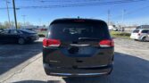 Back view of a black Pacifica minivan in a parking lot with power lines overhead under a clear blue sky.