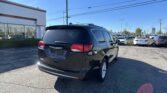 Rear view of a black SUV in a car dealership lot, with a white building to the left and rows of cars under a clear blue sky.