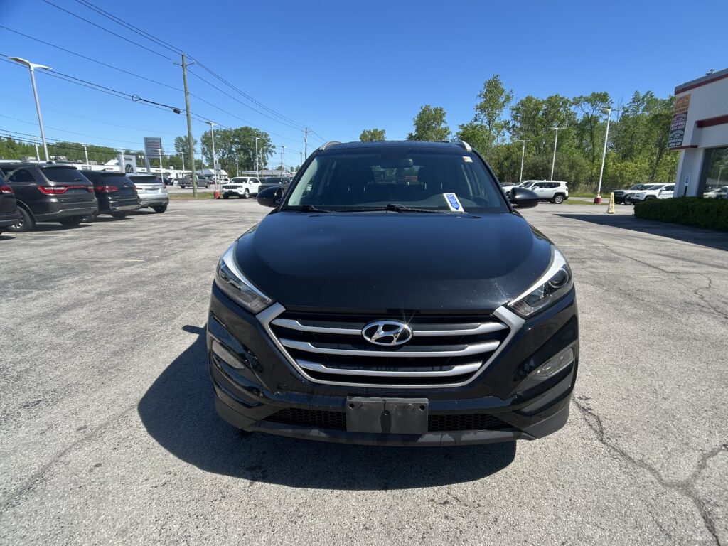 Front view of a dark blue Hyundai SUV in a parking lot with other cars and a dealership building in the background.