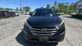 Front view of a dark blue Hyundai SUV in a parking lot with other cars and a dealership building in the background.