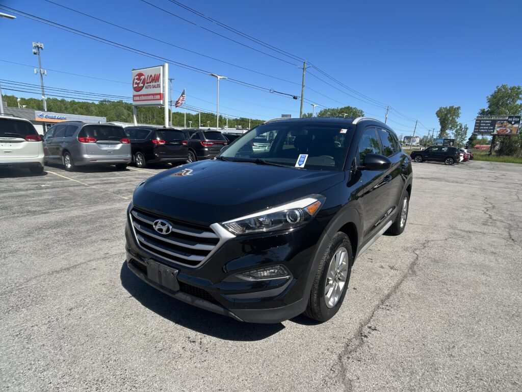 Front-right view of a black Hyundai SUV in a car dealership lot, with a row of minivans and an EZ LOAN Auto Sales sign in the background under a clear blue sky.