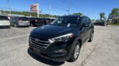 Front-right view of a black Hyundai SUV in a car dealership lot, with a row of minivans and an EZ LOAN Auto Sales sign in the background under a clear blue sky.