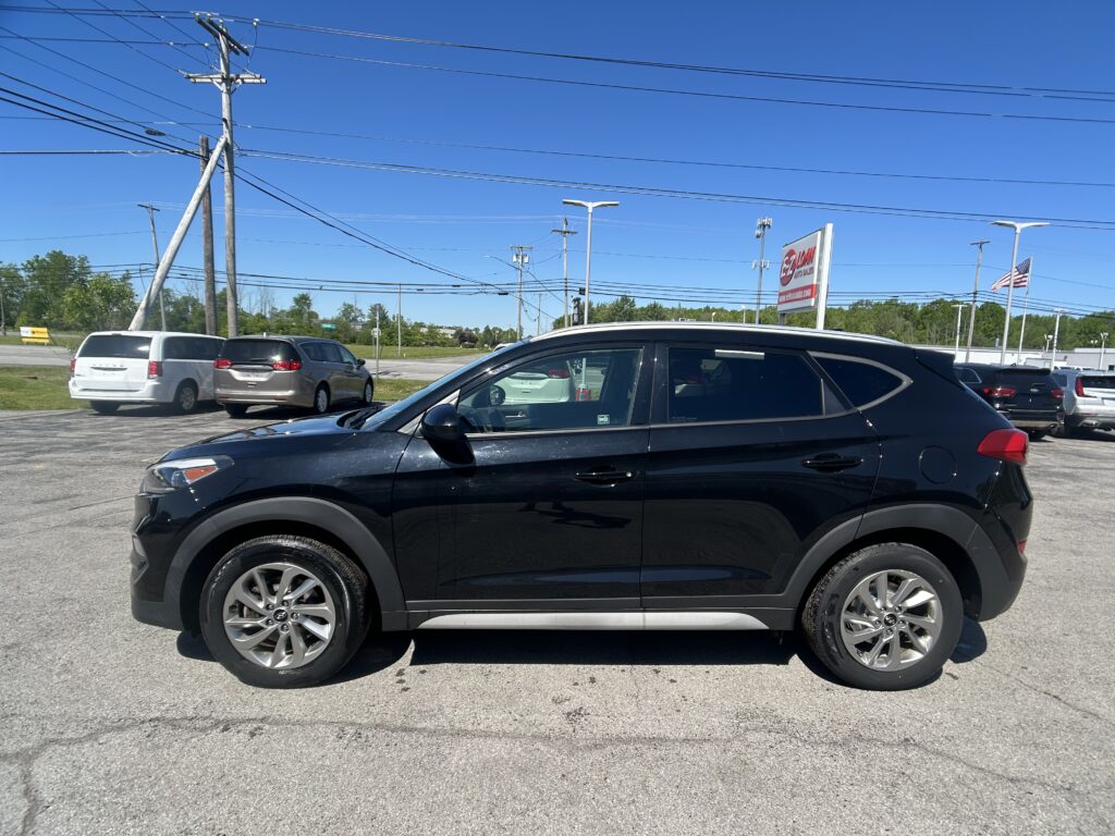 Black SUV in the foreground parked in a car dealership lot under power lines and a clear blue sky.