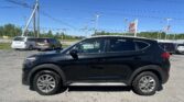 Black SUV in the foreground parked in a car dealership lot under power lines and a clear blue sky.