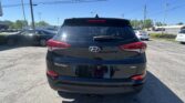 Rear view of a black Hyundai Tucson SUV in a parking lot on a sunny day, showing the AWD badge and red taillights.