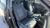 Front car interior with two black fabric seats, headrests, and center console visible. Non-driver side door is open, daylight entering.