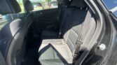 Back seat area of a dark car with three seats, headrests, and visible seat belts; outside parking lot with other vehicles through the window.