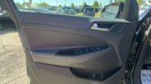 Driver-side car door interior with window controls; parking lot with many cars outside under a clear blue sky.