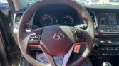 Driver's view of the car interior: steering wheel, instrument cluster, and center touchscreen display, with a parking lot outside the windshield.