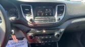 Car dashboard interior with center touchscreen showing 'AV Off' and surrounding controls; outside parking lot visible through windshield.