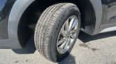 Close-up of a car wheel and tire mounted on the front fender, resting on asphalt surface
