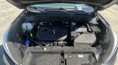 Front hood raised, view into the engine bay of a Hyundai SUV showing the coolant reservoir on the left, battery and fuse box on the right, and windshield wipers in the background in a parking lot
