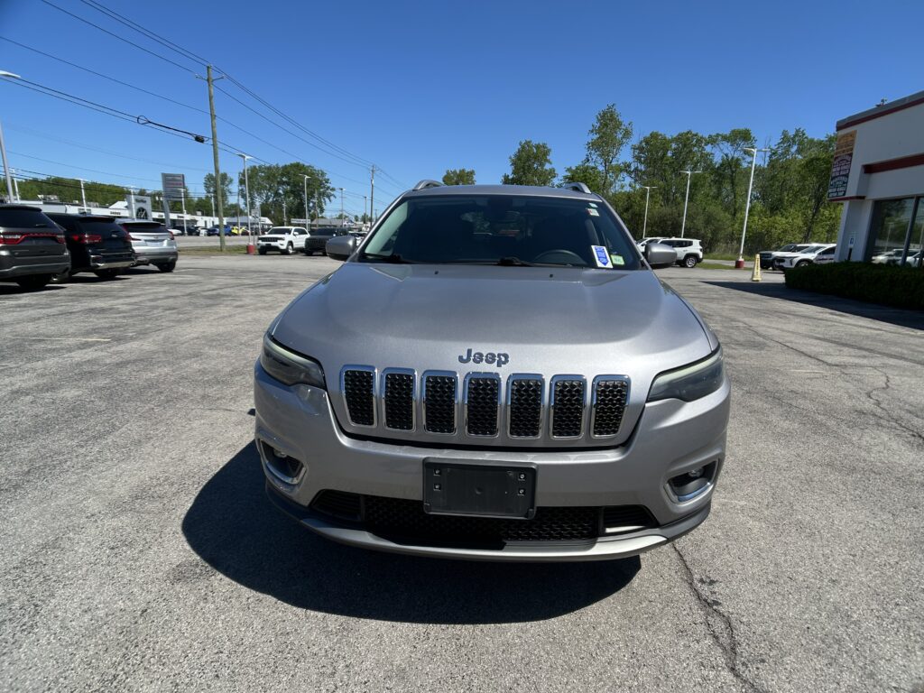 Front view of a silver Jeep SUV in a car dealership parking lot under a clear blue sky