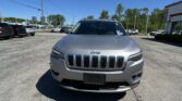 Front view of a silver Jeep SUV in a car dealership parking lot under a clear blue sky