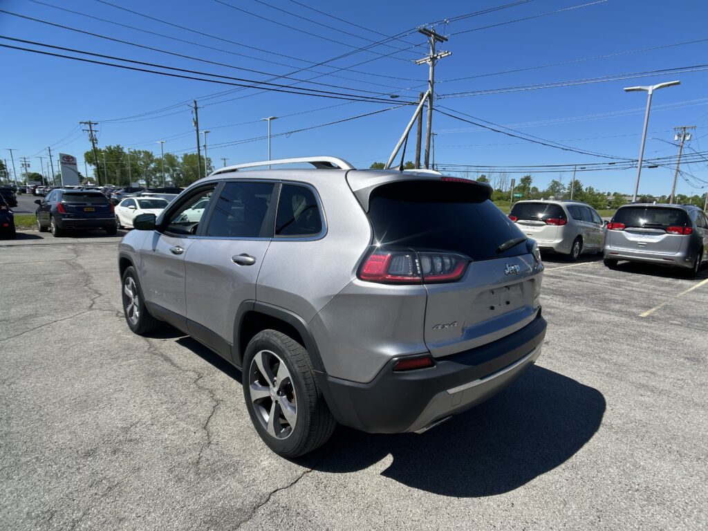 Silver SUV parked in a crowded car lot under a network of power lines against a bright blue sky.
