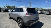 Silver SUV parked in a crowded car lot under a network of power lines against a bright blue sky.