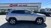 Silver SUV in the foreground at an auto dealership with an E-Z Loan Auto Sales sign on the building behind it, clear blue sky above.