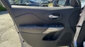 Inside view of a car door panel with window controls, mirror, and an open door; a busy dealer-ship parking lot is visible outside.