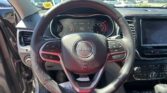 Interior view of a Jeep steering wheel and dashboard from the driver’s seat, with a bright parking lot visible through the windshield.