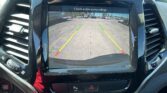 Car's infotainment screen displaying the rearview camera feed with guiding lines and 'Check entire surroundings' warning.