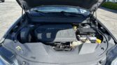 Open car hood showing engine bay with V6 VVT badge, battery, and coolant reservoir in a parking lot setting