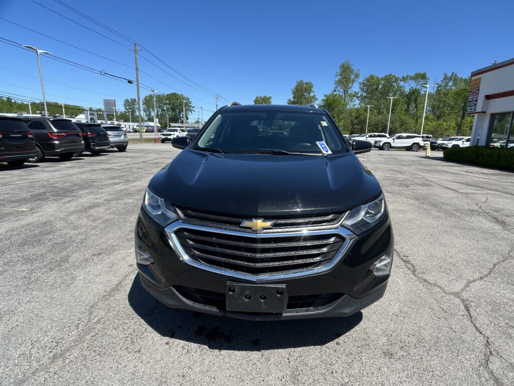 Front view of a black Chevrolet SUV in a sunny dealership parking lot with other cars in the background.