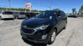 Black Chevrolet SUV in foreground at a car lot with other parked minivans and a tall EZ LOAN Auto Sales sign in the background on a sunny day