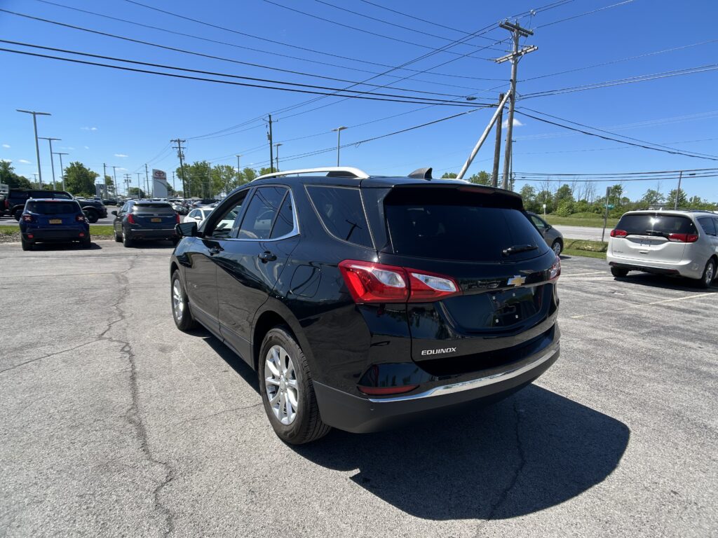 Rear three-quarter view of a black Chevrolet Equinox in a crowded parking lot on a sunny day with utility poles and power lines overhead.