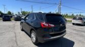 Rear three-quarter view of a black Chevrolet Equinox in a crowded parking lot on a sunny day with utility poles and power lines overhead.