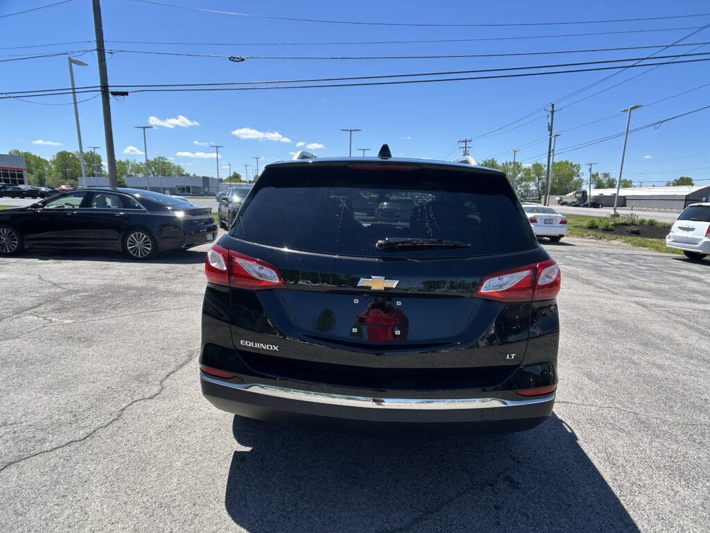 Rear view of a black Chevrolet Equinox LT parked in a lot with other cars and power lines overhead under a clear blue sky.