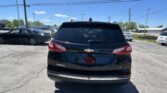 Rear view of a black Chevrolet Equinox LT parked in a lot with other cars and power lines overhead under a clear blue sky.