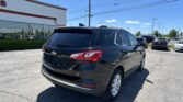 Black Chevrolet SUV parked in a car dealership lot with a white building and power lines in the background.