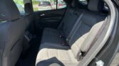 Rear car seat area with black fabric upholstery and visible seat belts, outside parking lot through open door window